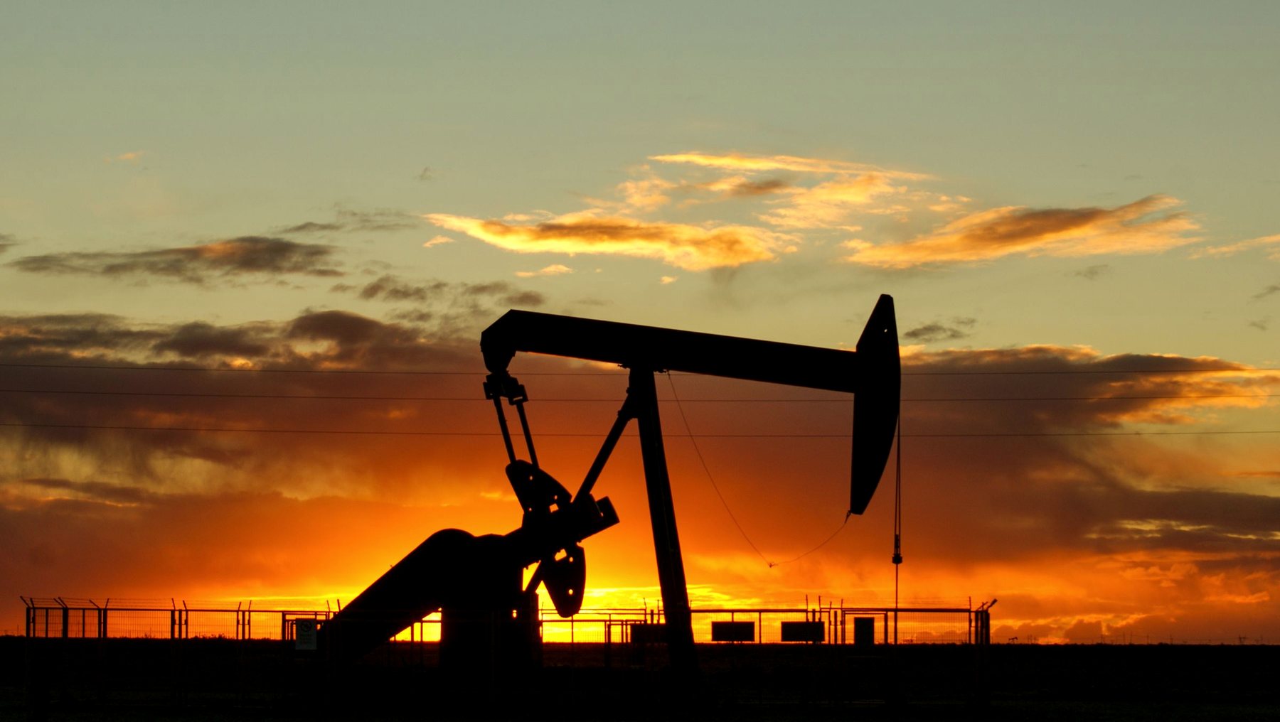 A pumping unit silhouetted against a desert sunset on a producing lease